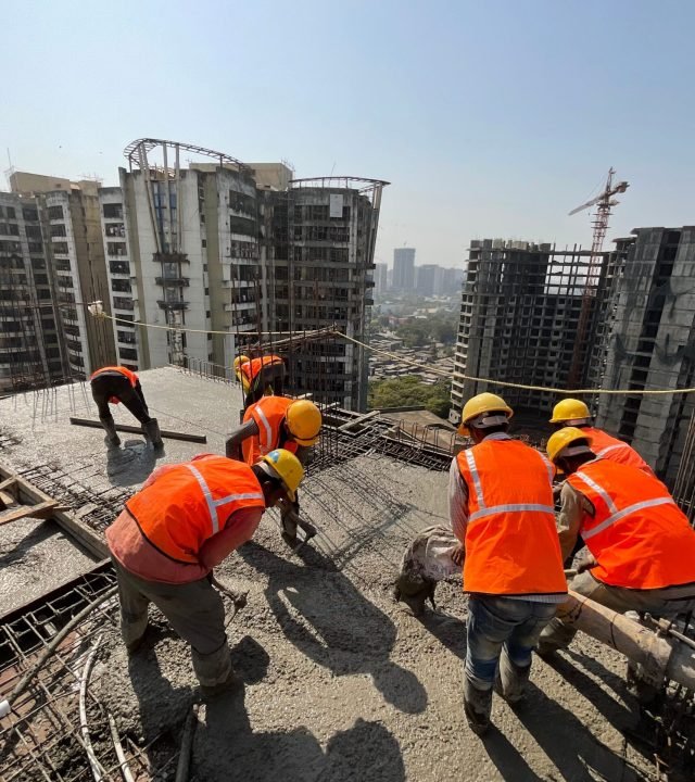 Workers in safety gear building a skyscraper with a city skyline backdrop.